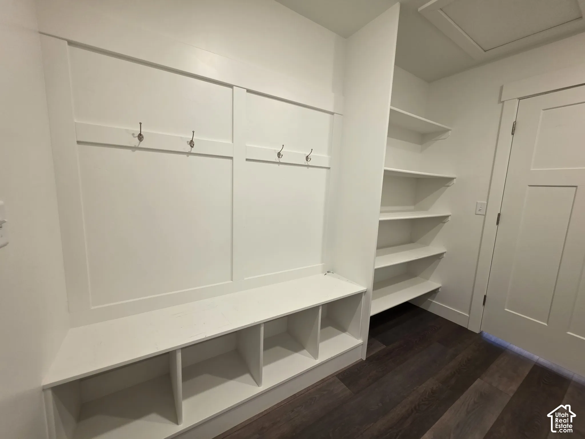 Built-in mudroom bench with cubby storage, integrated wall hooks, open shelving, and dark wood-finish flooring