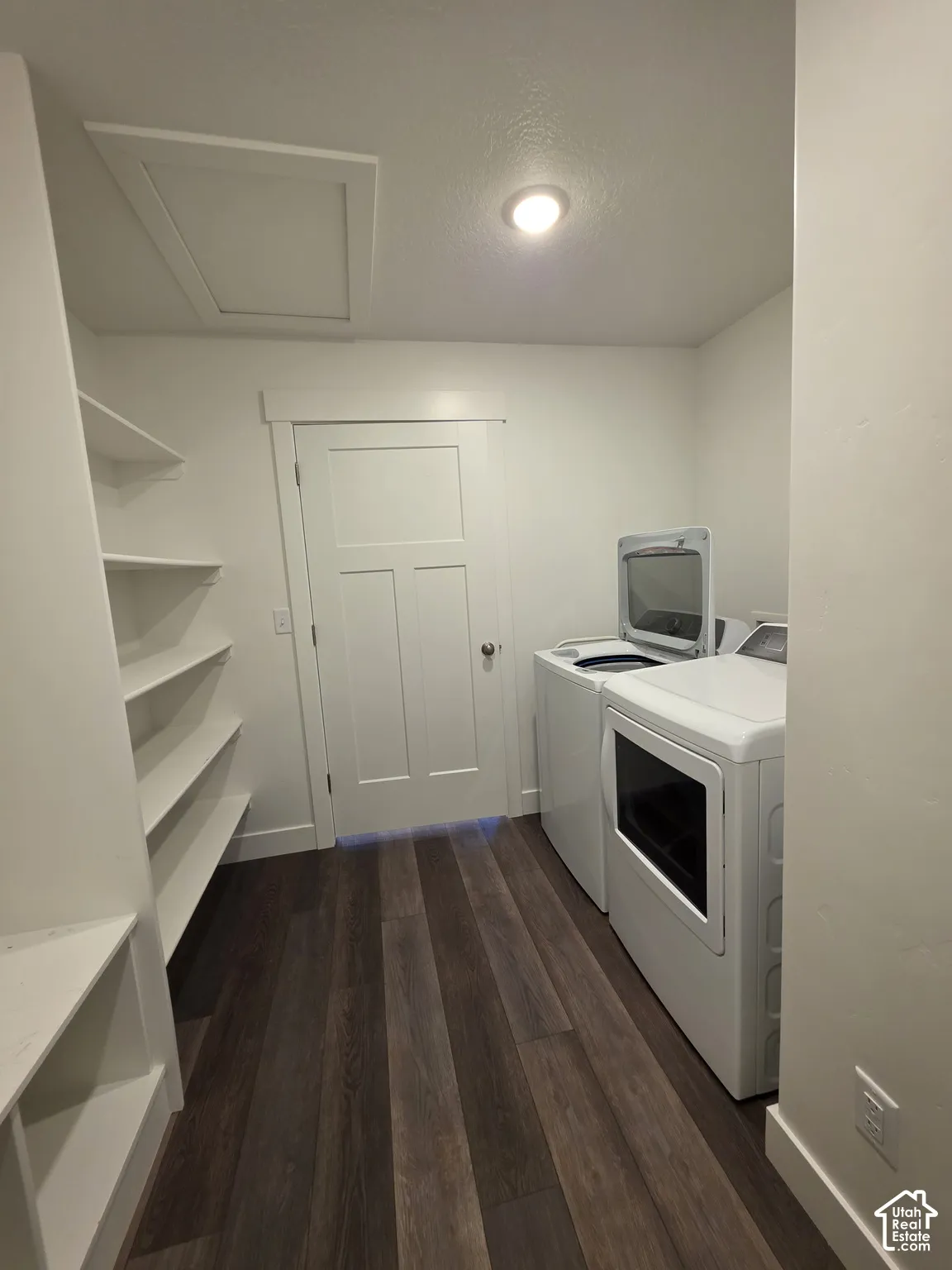 Laundry area featuring dark wood-finish flooring, white built-in shelving, white paneled door with brushed nickel hardware, and recessed ceiling lighting