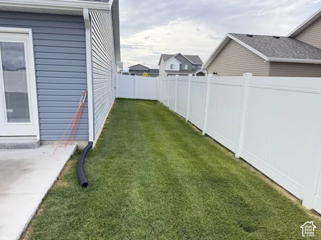 White vinyl fencing enclosing a grass lawn with a concrete patio and a siding exterior