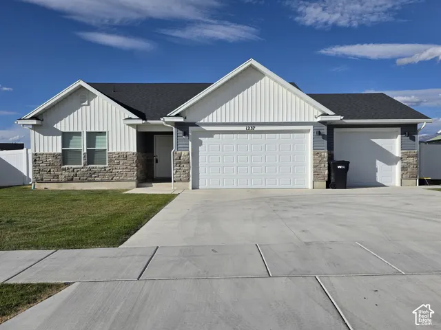 Modern ranch-style residence featuring a prominent two-car garage door, an additional single-car garage door, a stone and siding exterior, a dark shingled roof, and a concrete driveway
