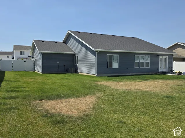 Rear exterior featuring dark gray siding, a charcoal shingle roof, and white vinyl fencing