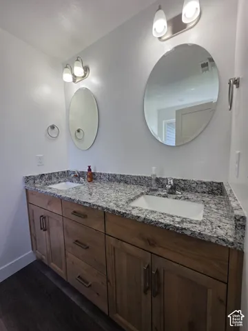 Dual vanity featuring a granite countertop with integrated sinks, wood-finish cabinetry, and contemporary lighting fixtures