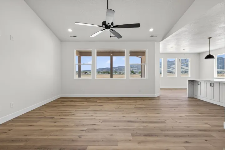 Spacious interior featuring pristine wood-finish flooring, white walls, and abundant natural light from expansive multi-pane windows framing mountain vistas