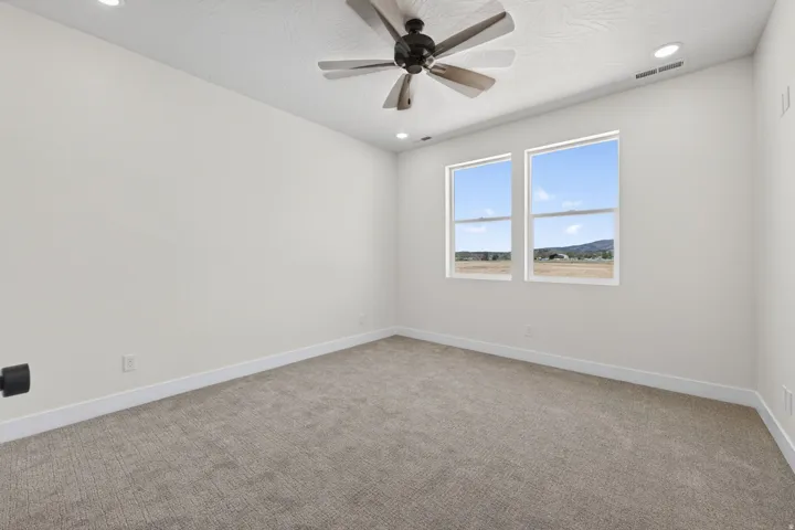 Bright and spacious bedroom featuring large dual windows with expansive natural light, neutral wall finishes, plush carpeting, ceiling fan with integrated lighting, and recessed ceiling lights