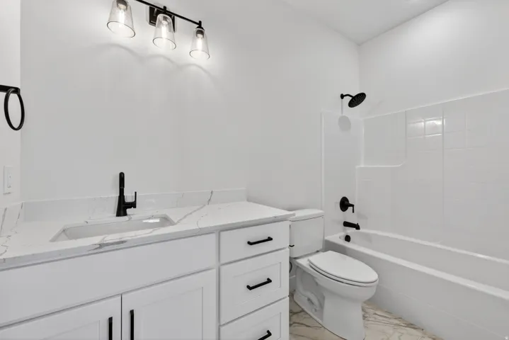 Modern bathroom featuring a white vanity with a quartz-finish countertop and integrated sink, matte black hardware, a tiled shower/tub combination, and contemporary lighting fixtures
