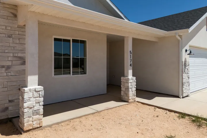 Modern covered patio featuring a spacious concrete foundation, large fixed-window with gridded panes, and decorative stacked stone pillars flanking the entrance