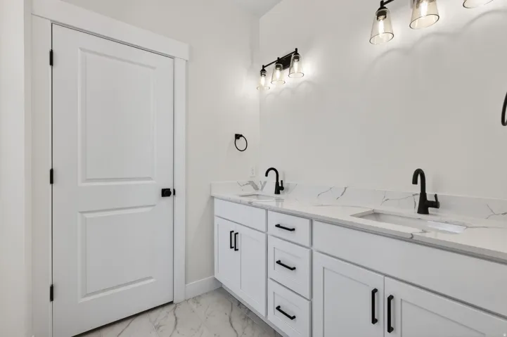 Spa-inspired dual-vanity bathroom featuring white cabinetry with soft-close drawers, marble-look countertops, and matte black faucet fixtures