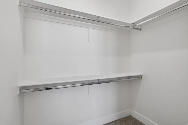 Spacious walk-in closet featuring dual chrome-finished hanging rods, white painted walls, and neutral flooring—ideal for organized storage and wardrobe display