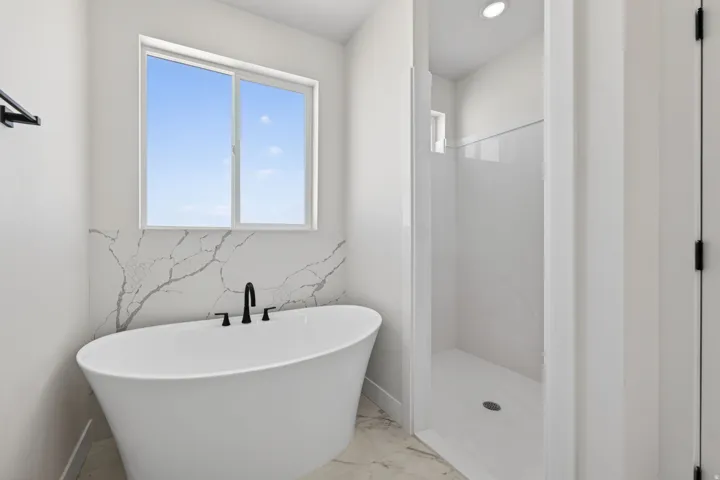 Spa-inspired primary bathroom featuring a freestanding soaking tub with matte black fixtures, marble-look tile backsplash, and polished concrete flooring