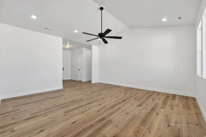 Spacious room showcasing wide-plank wood-finish flooring, recessed ceiling lighting, and a contemporary ceiling fan