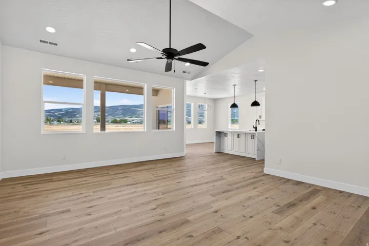 Spacious open-concept living area featuring wood-finish flooring throughout, recessed ceiling lighting, and a ceiling fan with brushed metal finish