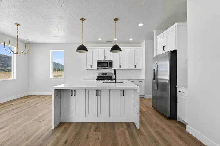 Open-concept kitchen featuring a waterfall island with a sink, white shaker cabinetry, stainless steel appliances, and wood-finish flooring