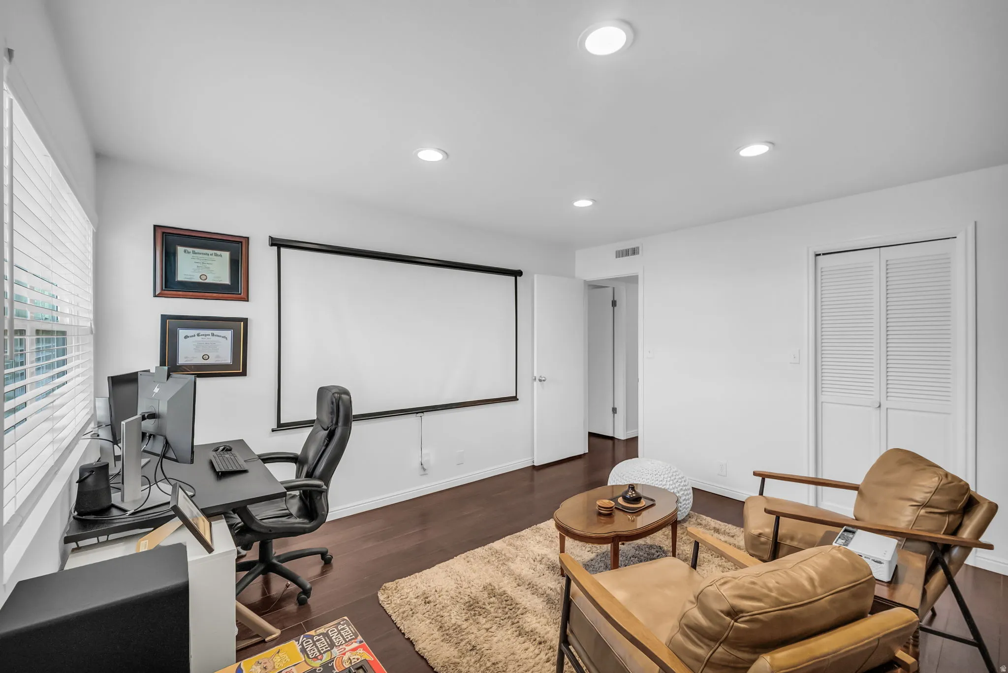 Versatile multi-purpose room featuring a large whiteboard wall, wood-finish flooring, recessed lighting, and dedicated workspace with ergonomic seating