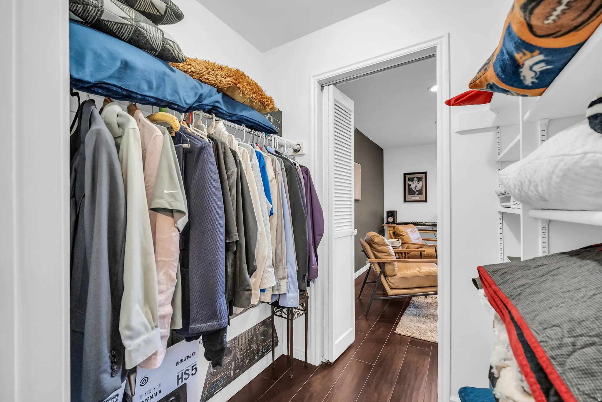 Spacious walk-in closet featuring a full-length clothing rod with multiple hanging sections, built-in shelving with woven storage baskets, and wood-finish flooring