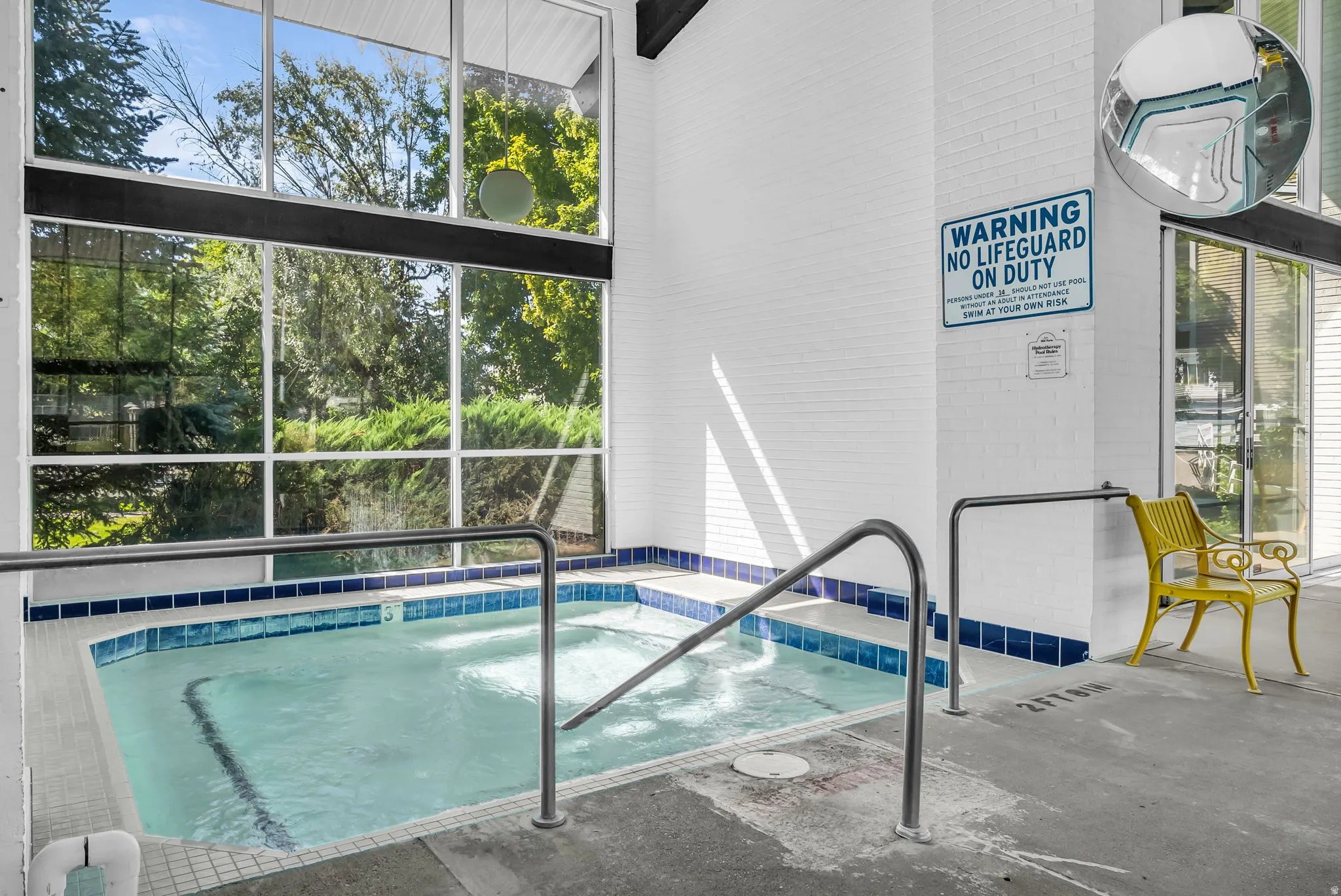 Indoor heated swimming pool with lap lane markings, navy tile accents, and metal handrails