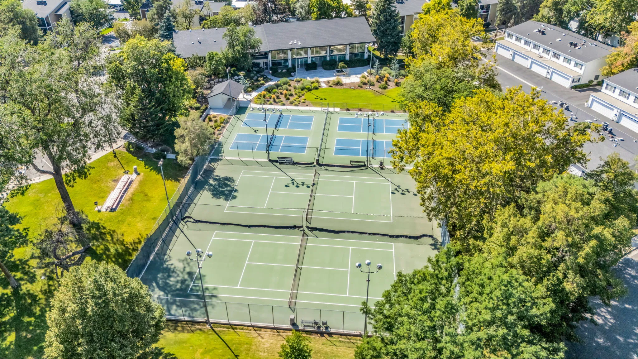 Multiple tennis courts with green surfacing and blue court markings, surrounded by mature trees