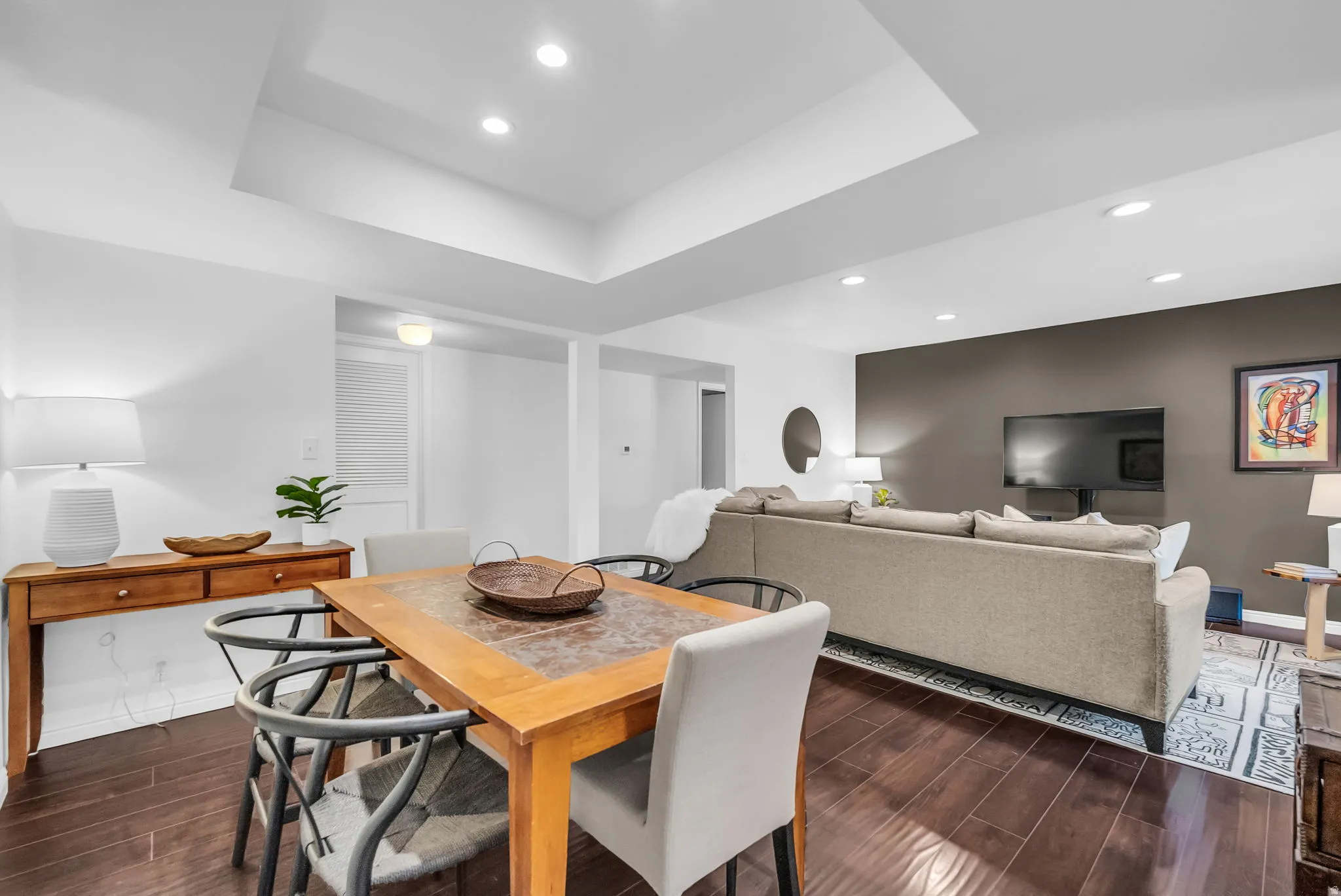 Open-concept living space featuring recessed lighting, dark wood-finish flooring, a tray ceiling, and a distinct accent wall