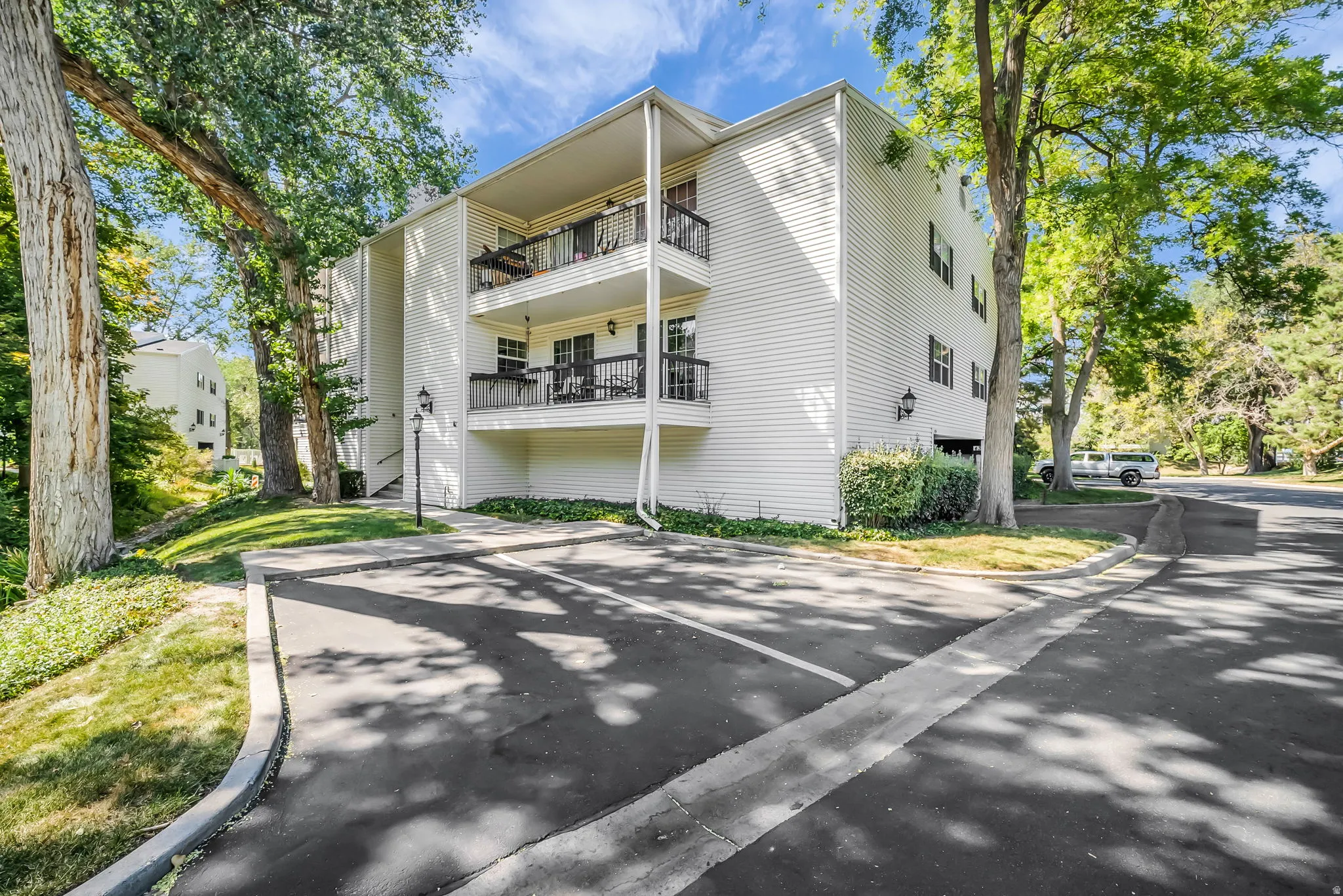 Modern three-story residential building featuring clean white vertical siding, multiple balconies with metal railings, and a structured architectural design