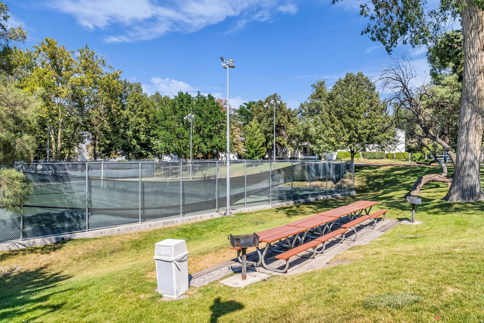 Expansive recreational grounds featuring a regulation-size tennis court with professional-grade fencing, mature landscaping with established trees, manicured lawn areas, and integrated seating