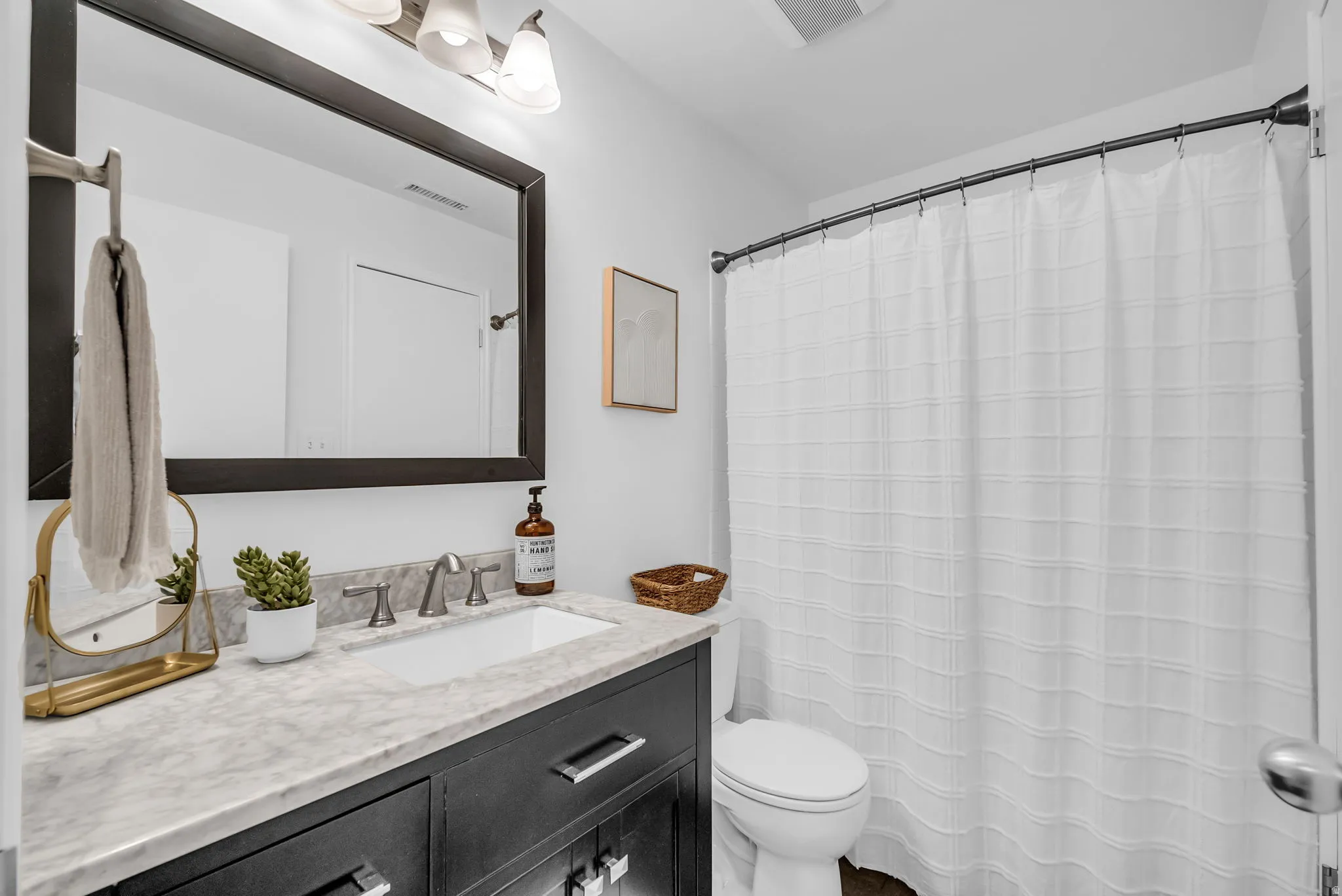 Spa-inspired bathroom featuring a dark vanity with marble-look countertop, dual sink configuration with polished chrome faucetry, and an oversized framed mirror with integrated lighting