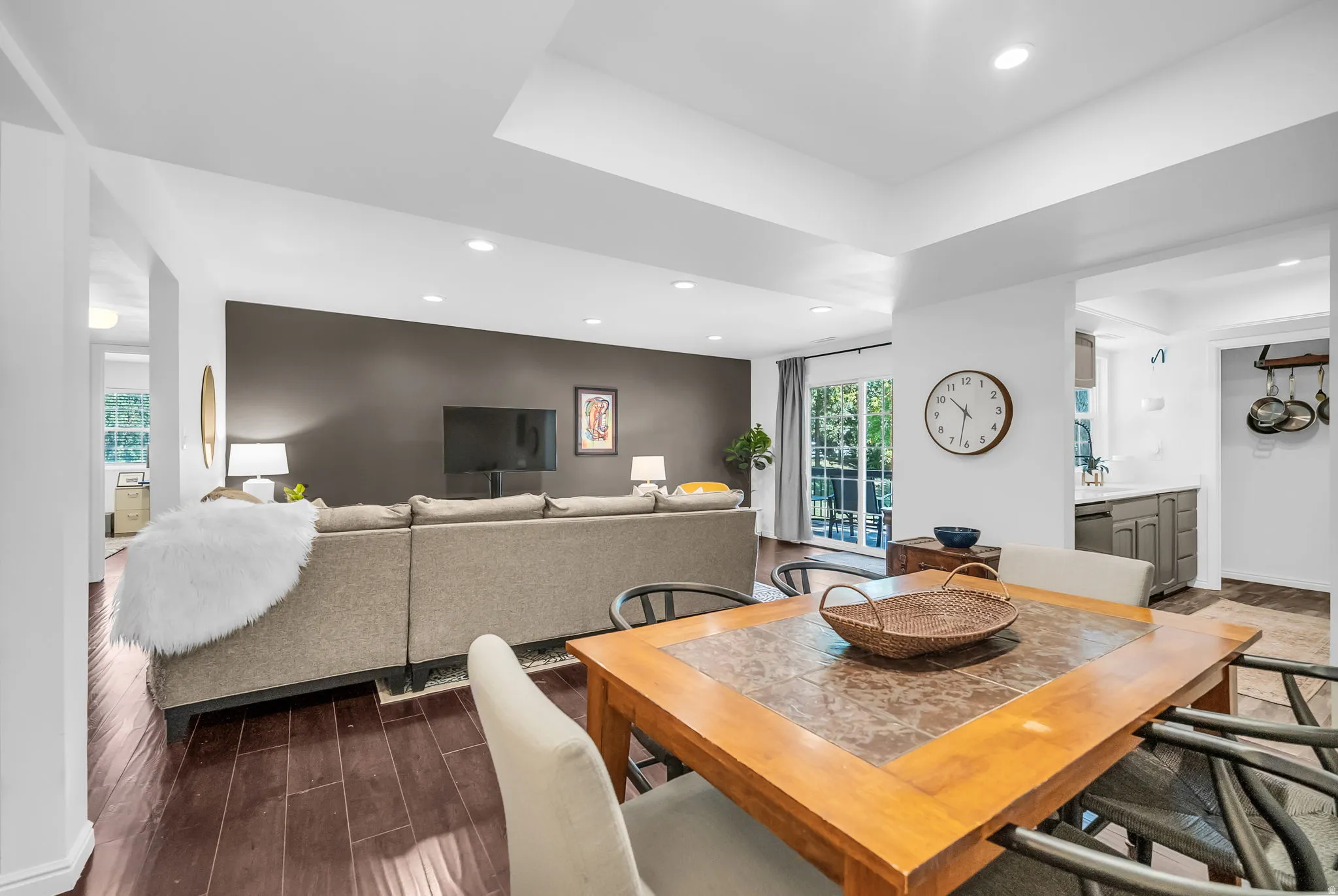 Open-concept living space featuring a wood-finish dining table with stone inlay top, neutral upholstered seating, and a dark accent wall with integrated media display
