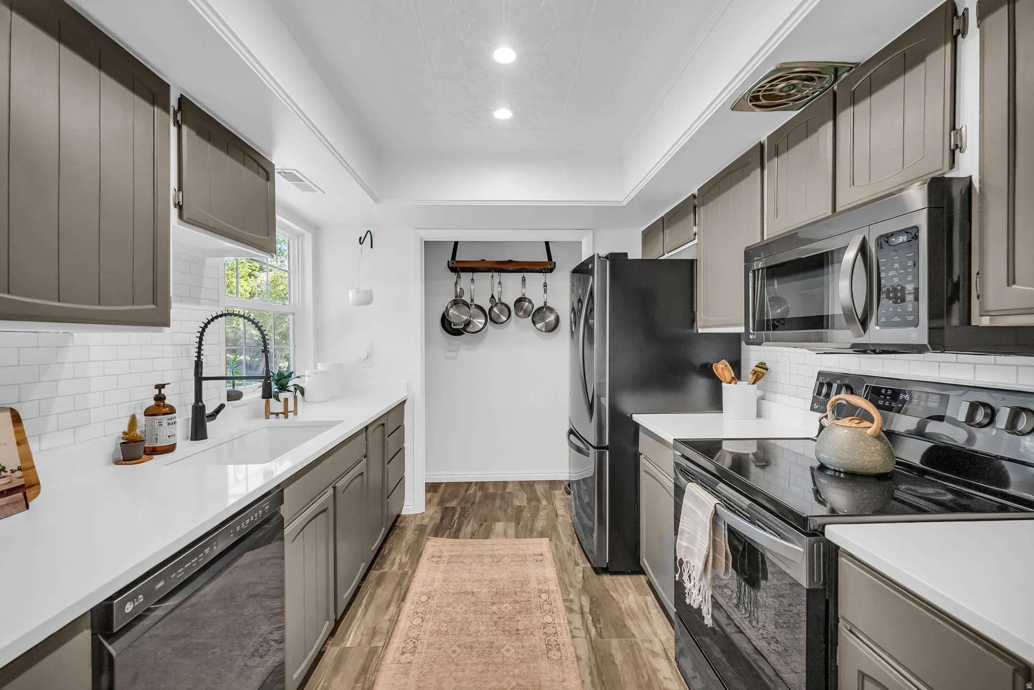 Galley-style kitchen featuring gray shaker cabinetry, white quartz countertops, and stainless steel appliances including a refrigerator, electric range, and microwave
