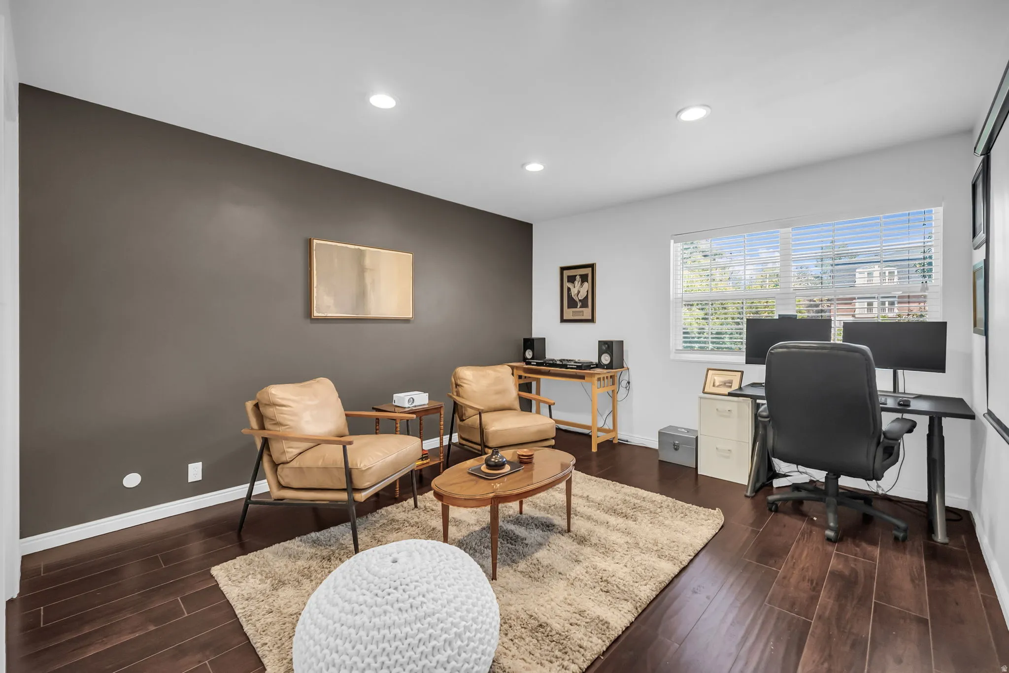 Contemporary home office featuring recessed ceiling lighting, warm wood-finish flooring, and a neutral color palette with an accent wall in charcoal gray