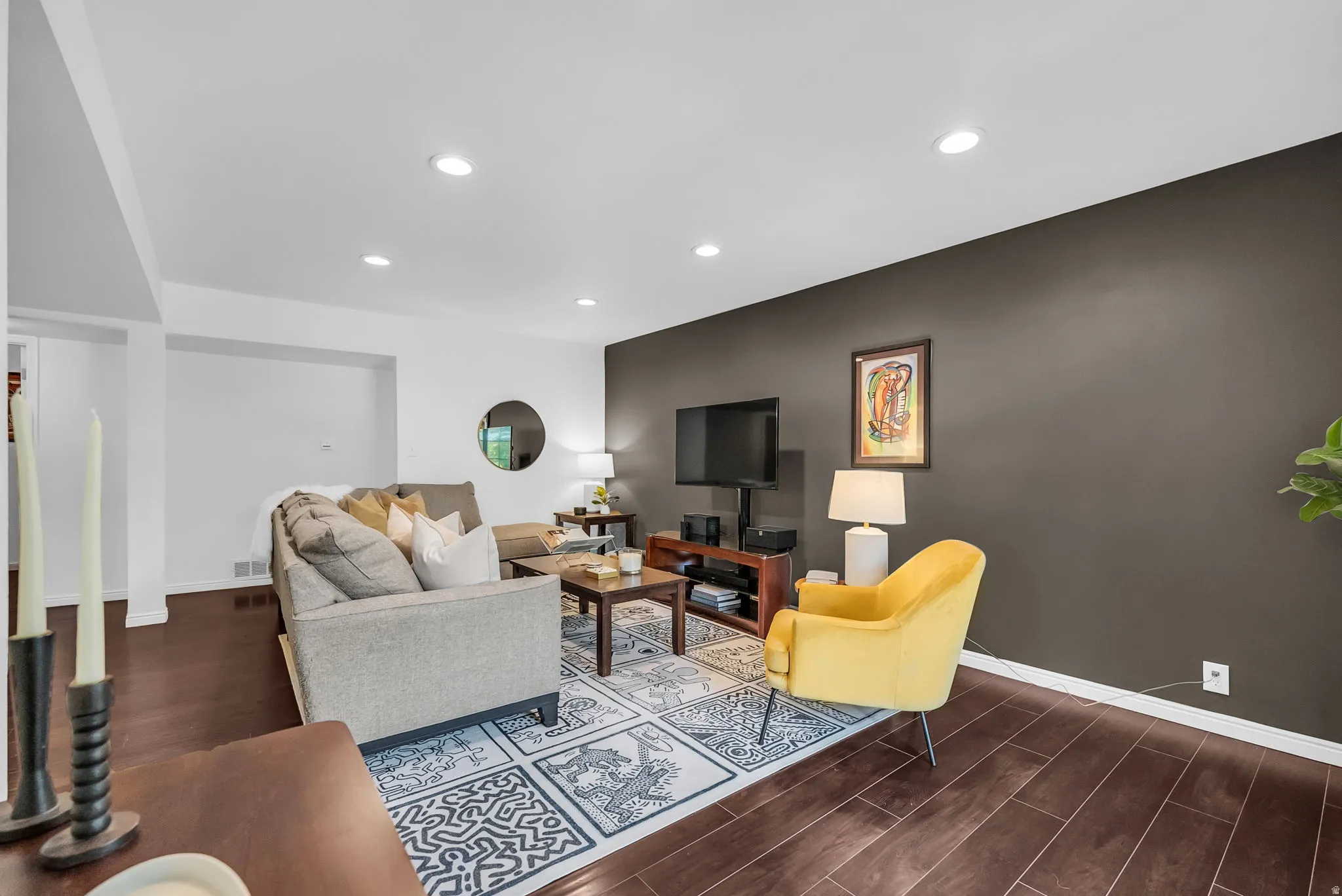 Sophisticated living room featuring a striking two-tone design with charcoal accent wall, recessed ceiling lighting, and dark wood-finish flooring throughout