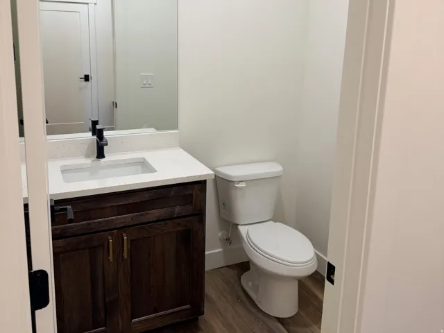 Powder room featuring wood-finish flooring, a dark wood vanity with a white countertop, an undermount sink, and a black faucet