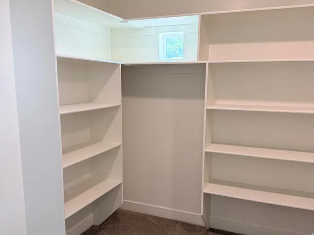 Built-in shelving system with ample storage space, a high-set window, baseboard trim, and carpeted flooring