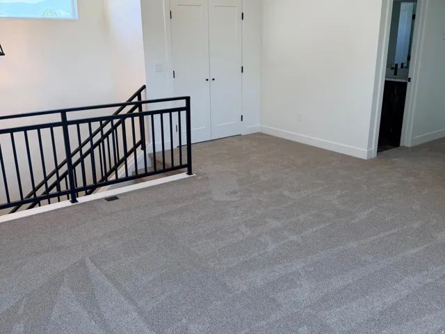 Upper-level space featuring light gray carpeting, crisp white walls, and a contemporary black metal stair railing