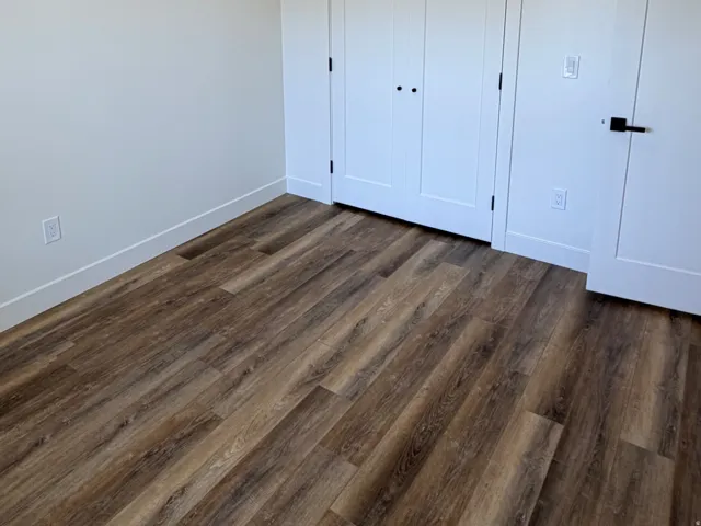 Spacious room featuring wood-finish flooring, white baseboards, and a double-door closet with trim