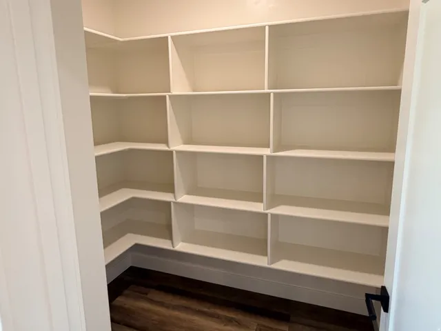 Spacious pantry featuring extensive built-in white shelving, wood-finish flooring, and recessed ceiling lighting