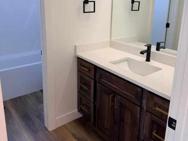 Bathroom featuring a dark wood-finish vanity with a light countertop, an integrated sink, and matte black fixtures