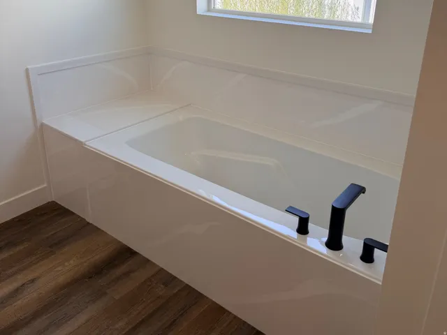 Built-in bathtub with black fixtures, wood-finish flooring, and a large window