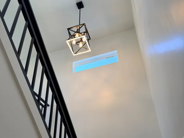 Modern geometric chandelier illuminating a two-story entryway with a high transom window, sleek black staircase railing, and contemporary wall finishes