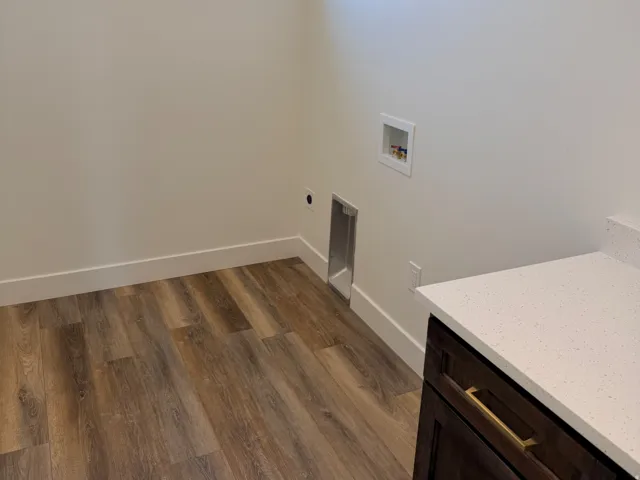 Laundry area featuring wood-finish flooring, a rectangular transom window, and a built-in dark wood-finish cabinet with a light-toned countertop and gold-tone hardware