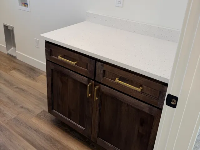 Dark wood-finish cabinetry with gold-tone hardware, white countertop, and wood-finish flooring