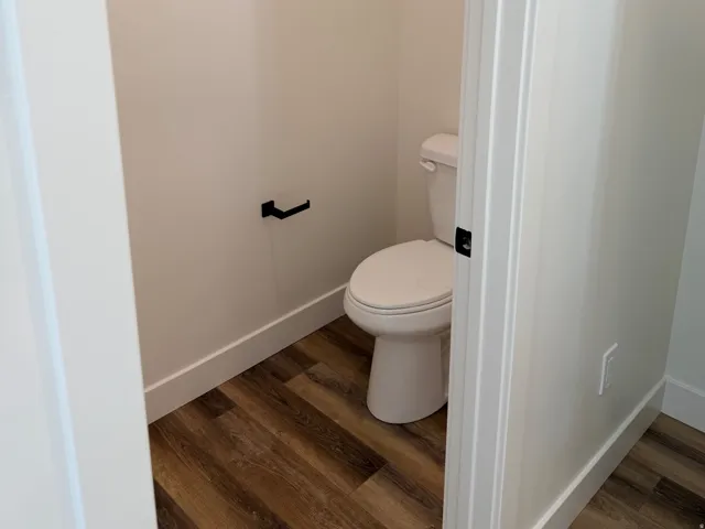 Powder room featuring wood-finish flooring, white baseboards, and a white toilet