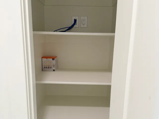 Built-in shelving unit featuring multiple white shelves, a wall outlet, and a data port