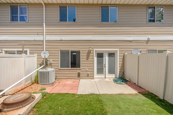 Rear exterior featuring tan siding, a ground-level concrete patio, and a private fenced yard with green lawn