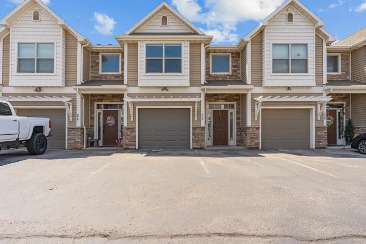 Multi-level townhome exterior featuring an attached garage, stone veneer accents, horizontal siding, and multiple windows