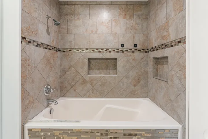Bathtub with a tiled surround featuring a decorative mosaic accent stripe