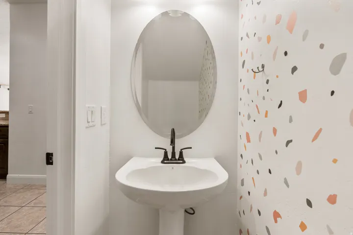 Pedestal sink with a matte black faucet, complemented by an oval mirror and recessed lighting