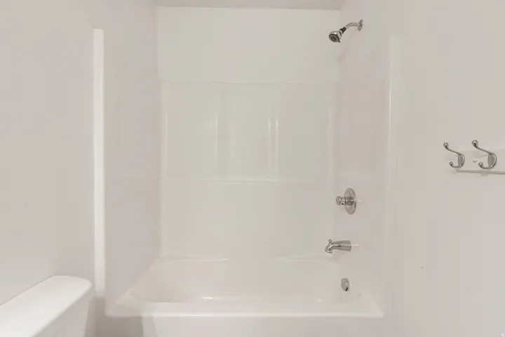 White bathtub with integrated shower, featuring a chrome showerhead and control hardware, and a tile-patterned surround