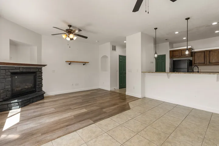 Open-concept living area featuring a stone fireplace, wood-finish flooring, and a kitchen pass-through with pendant lighting
