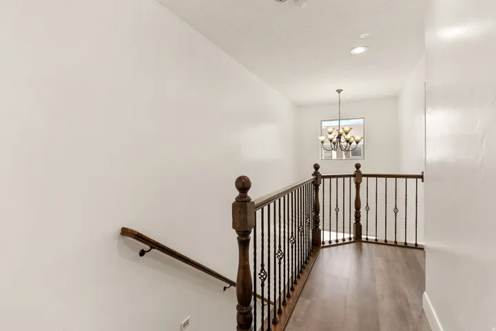 Upper landing featuring wood-finish flooring, a wrought iron and wood baluster railing, and a multi-arm chandelier