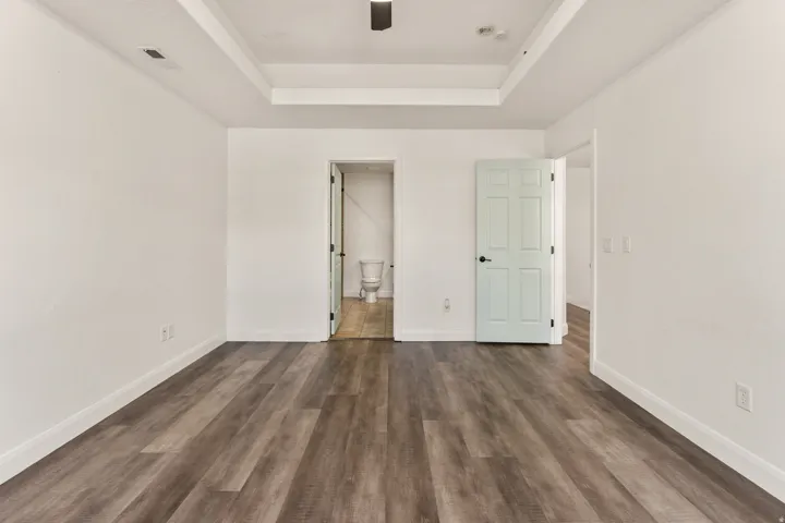 Spacious room featuring wood-finish flooring, white walls, and a tray ceiling