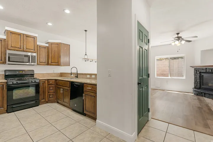 Kitchen featuring wood cabinetry, stone countertops, black appliances, and tile flooring