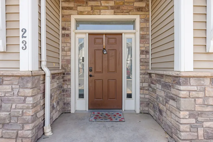 Entryway featuring a brown panel door with transom window and sidelights, complemented by stacked stone veneer accents and tan horizontal siding